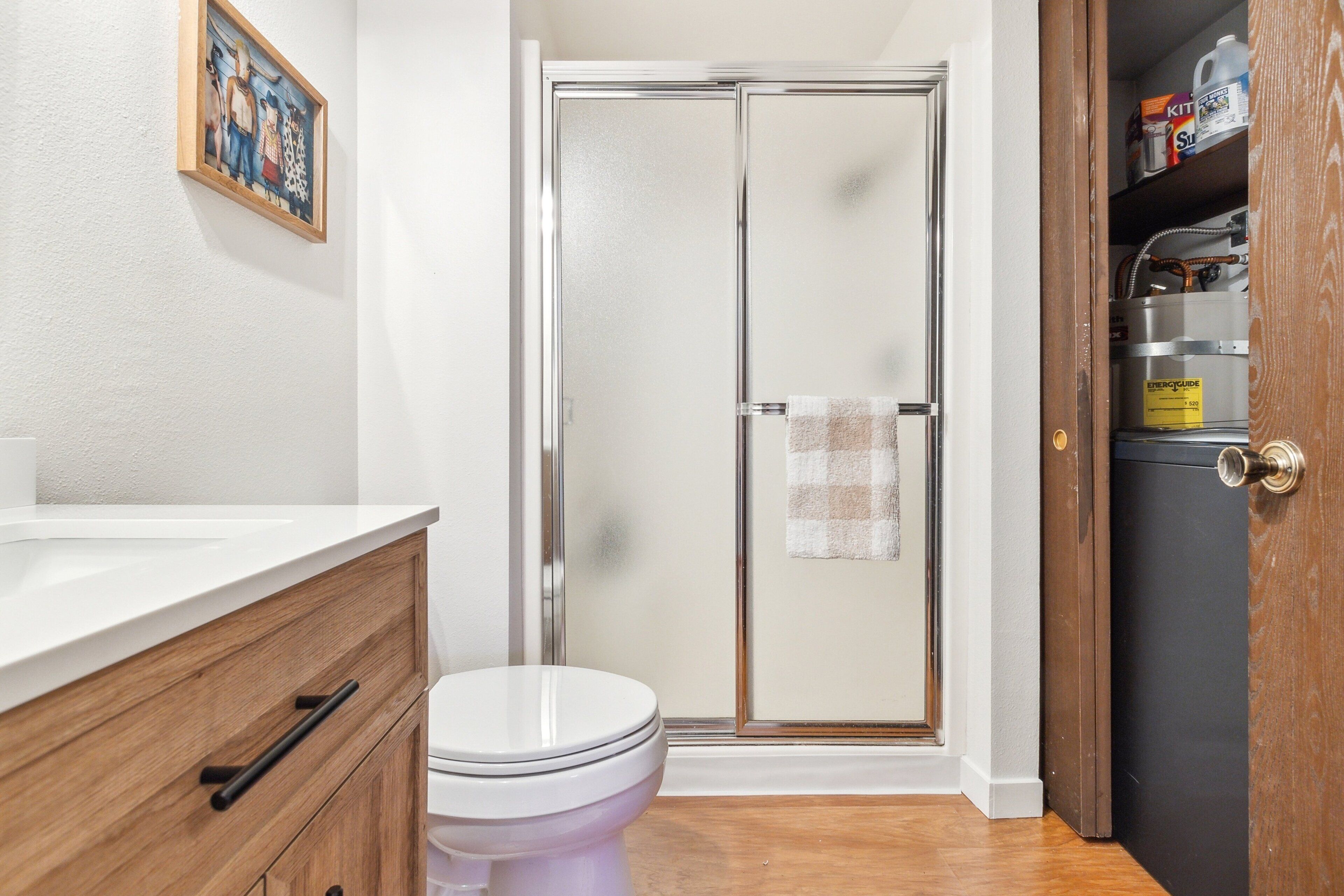 Un bagno con box doccia in vetro, un WC bianco, un mobile bagno in legno con un cassetto e uno scaffale con articoli da toilette.