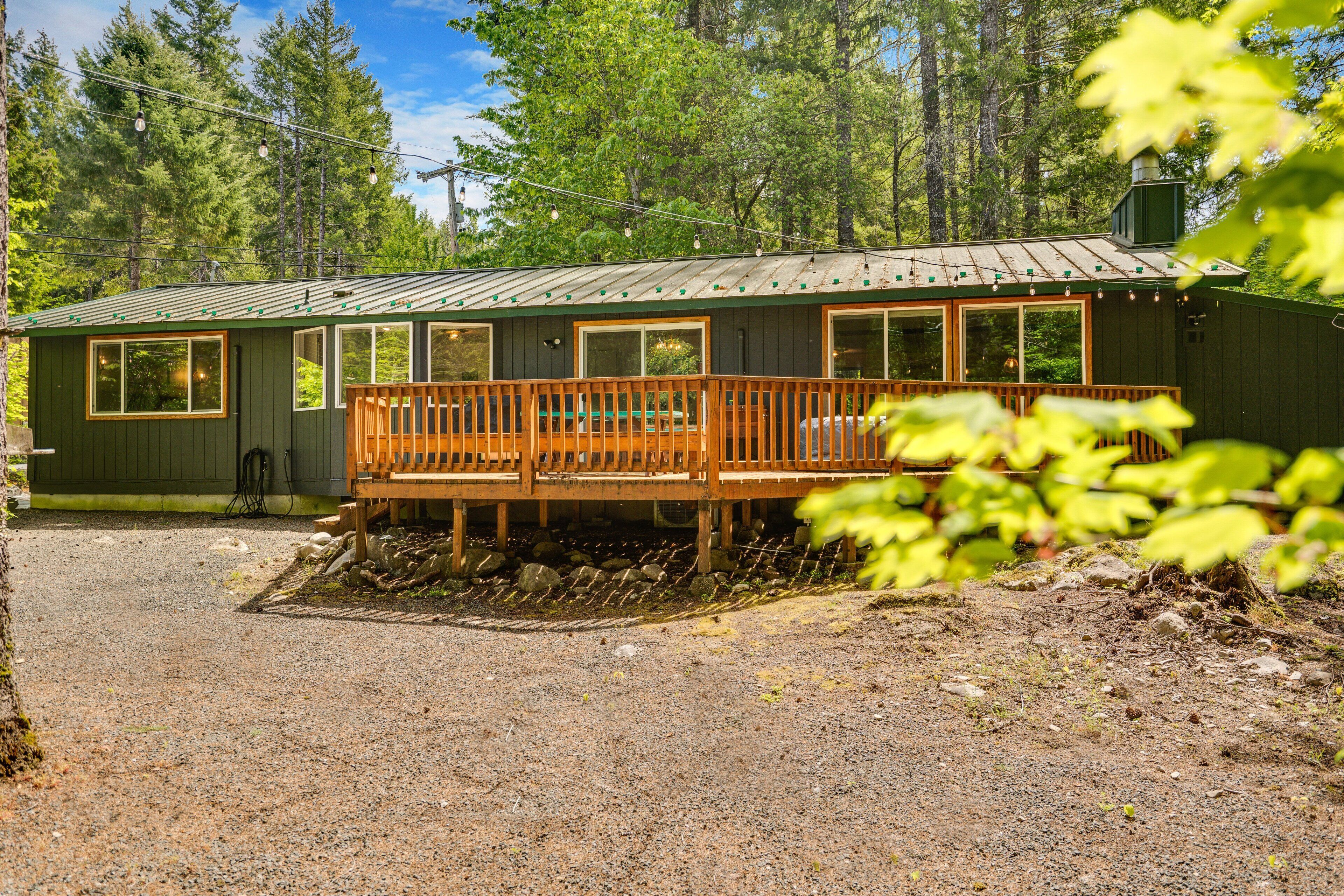 A cabin with a wooden deck, large windows, and a metal roof, surrounded by trees.