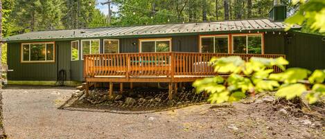 A cabin with a wooden deck, large windows, and a metal roof, surrounded by trees.