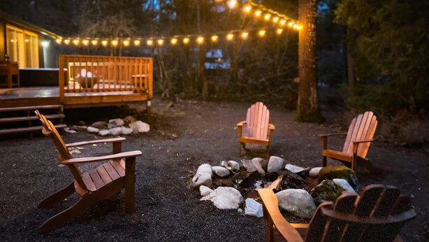 A cozy outdoor seating area with Adirondack chairs and a fire pit, surrounded by a deck and string lights.