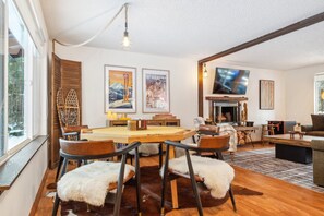 A cozy living room with a fireplace, a television, and a dining area with a wooden table and chairs. - Packshack - Cozy Ski Cabin Mins From White Pass 2 Bedroom Home (Packwood)