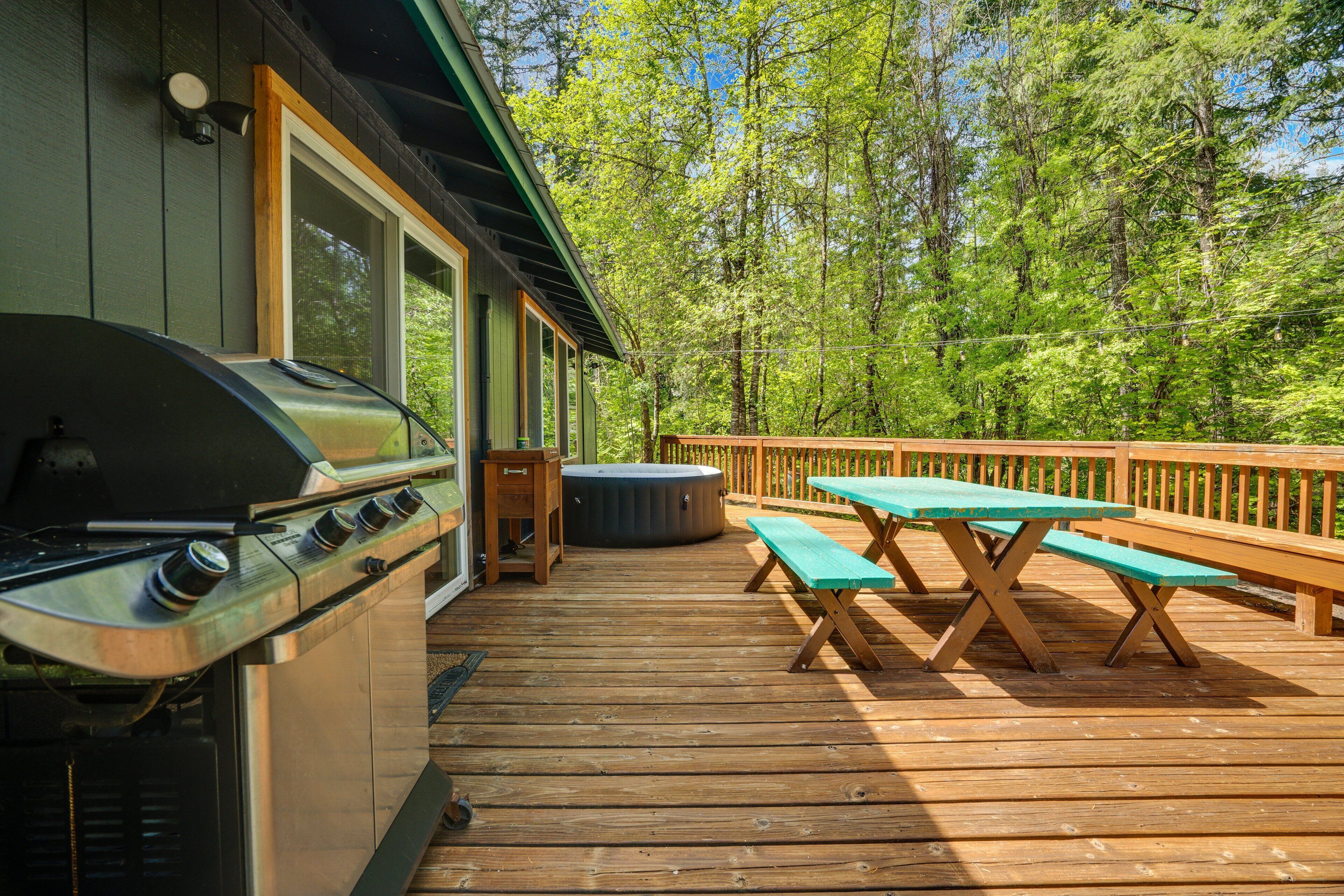 Eine Holzterrasse mit Grill, Picknicktischen und einem Whirlpool.