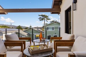 A balcony with two wooden chairs, a small round table with a tray of breakfast items, and a view of neighboring houses.