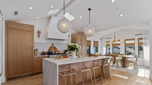 Une cuisine moderne dotée d’un îlot central, de tabourets de bar, de luminaires suspendus et offrant une vue sur l’extérieur.