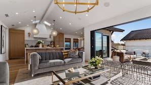 Un espace de vie moderne avec un canapé gris, une table basse en verre, des meubles en osier et une cuisine en arrière-plan.