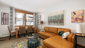 A living room with a brown sofa, a glass coffee table, wicker chairs, a patterned rug, and artwork on the walls. - Premium Unit 1305 - Zephyr Mountain Lodge 1 Bedroom Condo (Winter Park)