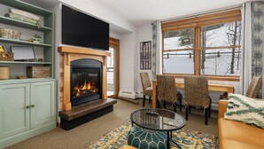 A cozy living room with a fireplace, comfortable seating, and a large window with a view of a snowy landscape. - Premium Unit 1305 - Zephyr Mountain Lodge 1 Bedroom Condo (Winter Park)