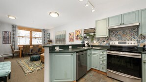 A spacious kitchen with light blue cabinets, a stainless steel dishwasher, and a large oven. There is a dining area with a table and chairs, and a window providing natural light. - Premium Unit 1305 - Zephyr Mountain Lodge 1 Bedroom Condo (Winter Park)