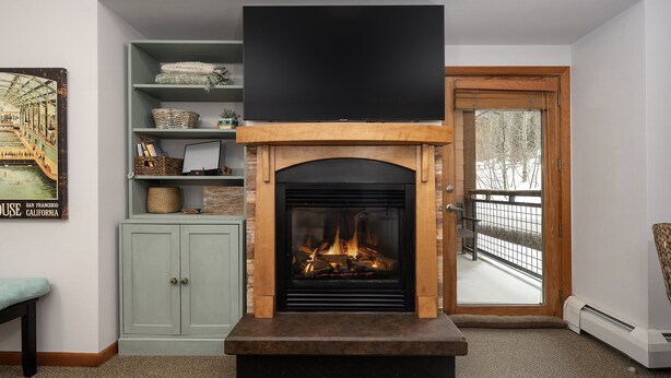 A living room with a fireplace, a television mounted above it, and a bookshelf with various items. - Premium Unit 1305 - Zephyr Mountain Lodge 1 Bedroom Condo (Winter Park)