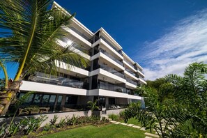 A multi-story building with balconies, a garden area, and a clear blue sky.
