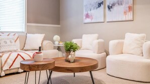 A modern living room with a sofa, two armchairs, a coffee table, and abstract wall art. - Marbella Lane - Charming 4BR Bungalo for Relaxing Retreat (Fullerton)