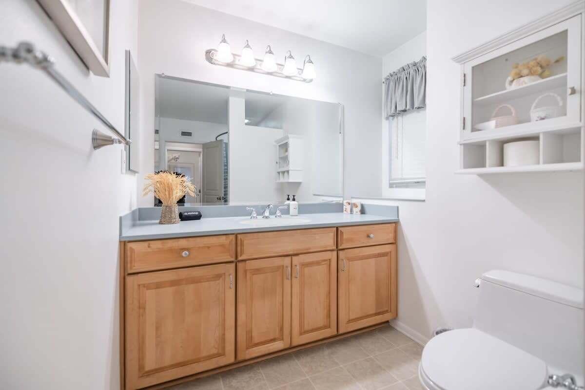 Une salle de bain avec un meuble-lavabo en bois, un grand miroir et des toilettes blanches.