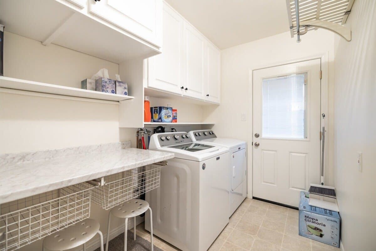 A laundry room with a washing machine, dryer, and a countertop with shelves.