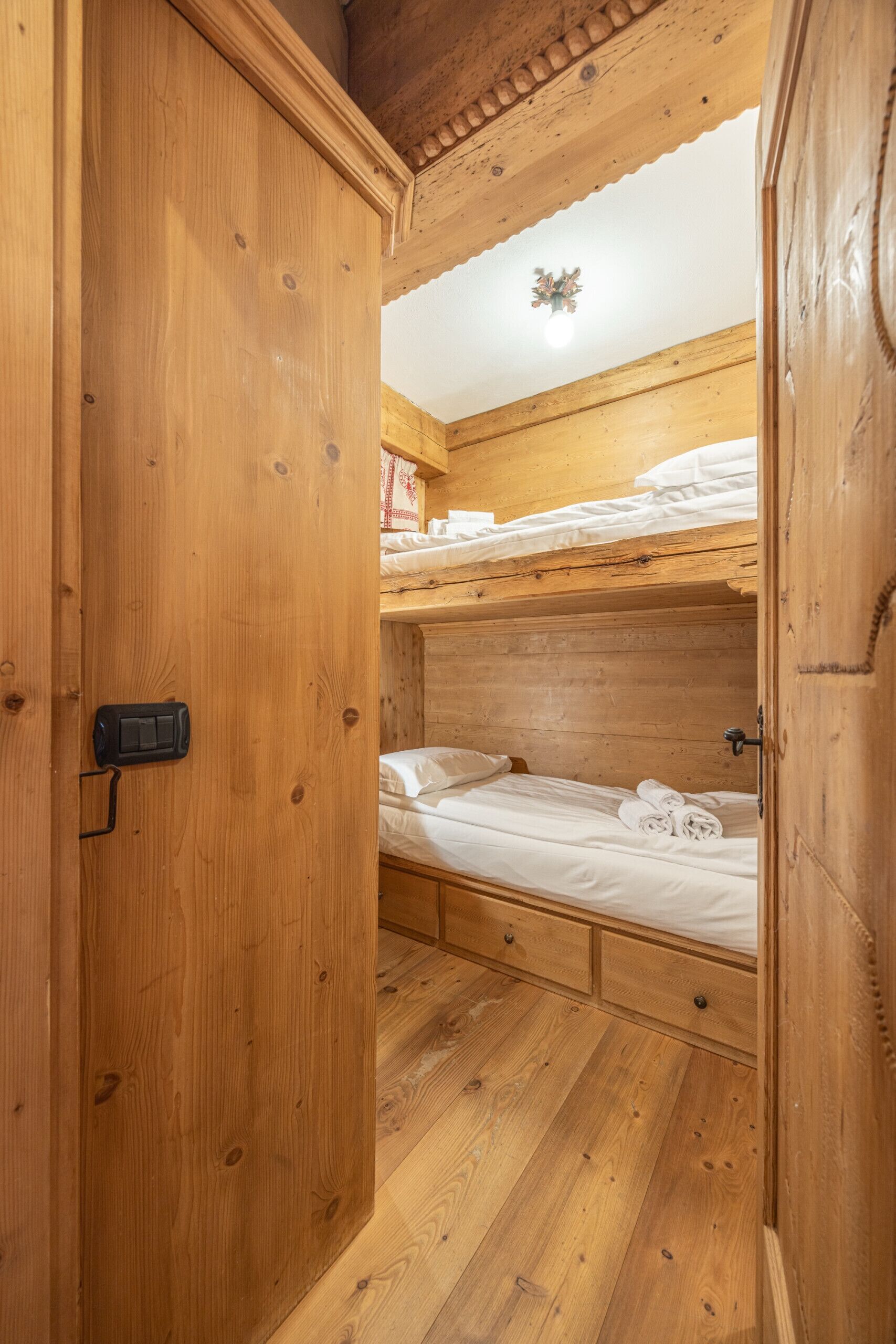 Une pièce en bois avec un lit superposé, une porte en bois dotée d’une poignée et un luminaire fixé au plafond.