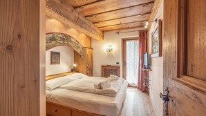 A wooden room with a bed, a small table, a wall-mounted TV, and a door. - Casa Col, near the ski slopes with view of the Dolomites (Cortina d´Ampezzo)
