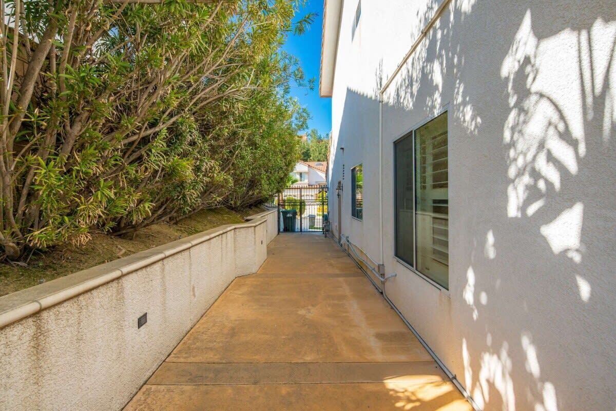 A narrow concrete pathway flanked by a white building and dense greenery.