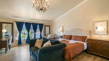 Camera d'hotel con un letto grande, una poltrona, un comò e un lampadario.