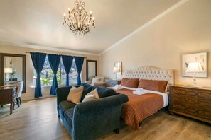 Camera d'hotel con un letto grande, una poltrona, un comò e un lampadario.