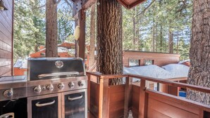 A rustic cabin with a wood-burning stove, a grill, and a view of the surrounding forest. - Winterset Luxe 2 bedroom+Loft in the heart of Mammoth Lakes (Mammoth Lakes)