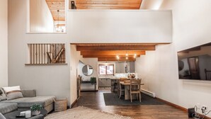 A spacious living area with a high ceiling, wooden beams, a dining area with a wooden table and chairs, and a kitchen in the background. - Winterset Luxe 2 bedroom+Loft in the heart of Mammoth Lakes (Mammoth Lakes)