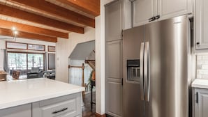 A modern kitchen with a stainless steel refrigerator, wooden ceiling beams, and a view of the outdoors through large windows. - Winterset Luxe 2 bedroom+Loft in the heart of Mammoth Lakes (Mammoth Lakes)