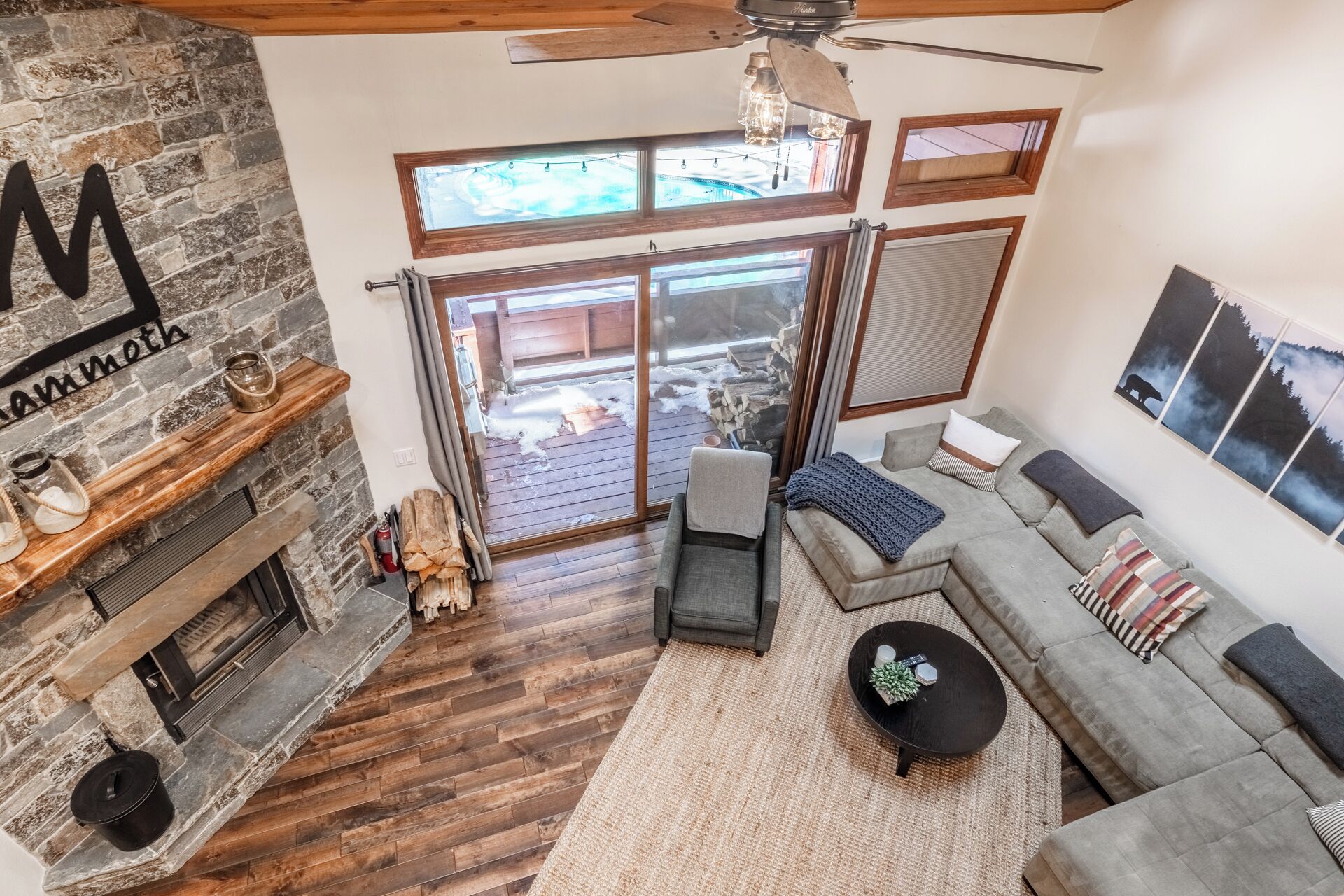 Un salon chaleureux avec une cheminée, un mur en pierre, une grande fenêtre et un ventilateur de plafond.