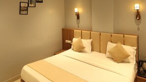A bedroom with a large bed, a ceiling fan, wall-mounted lights, and framed artwork on the wall. - Hotel Trinay (Jaipur)