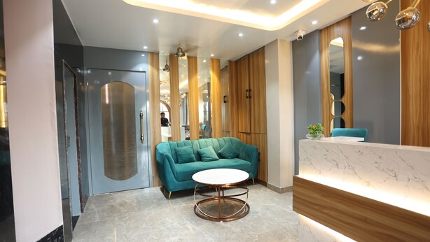 A modern reception area with a marble reception desk, a teal sofa, and a round table. - Hotel Trinay (Jaipur)