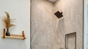 Un baño con pared de mármol, cabezal de ducha y una pequeña repisa con un jarrón y una caja.