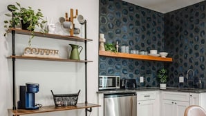 Una cocina moderna con armarios blancos, un lavavajillas de acero inoxidable, un microondas y una cafetera sobre un estante de madera.