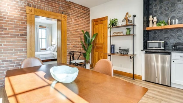 Una cocina moderna con pared de ladrillo, puerta de madera y una zona de comedor con mesa y sillas.