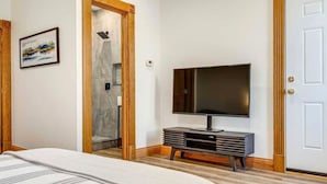Habitación de hotel con una cama grande, un televisor sobre un soporte de madera, ducha y una puerta con marco decorativo.