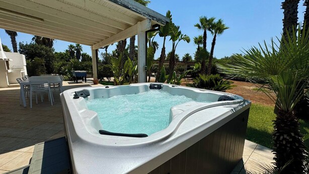 A hot tub with a wooden deck and chairs, surrounded by palm trees and a covered patio area. - Villa Malaspina - Hot Tub, 3 Bedrooms, Sleeps 6 (Alliste)