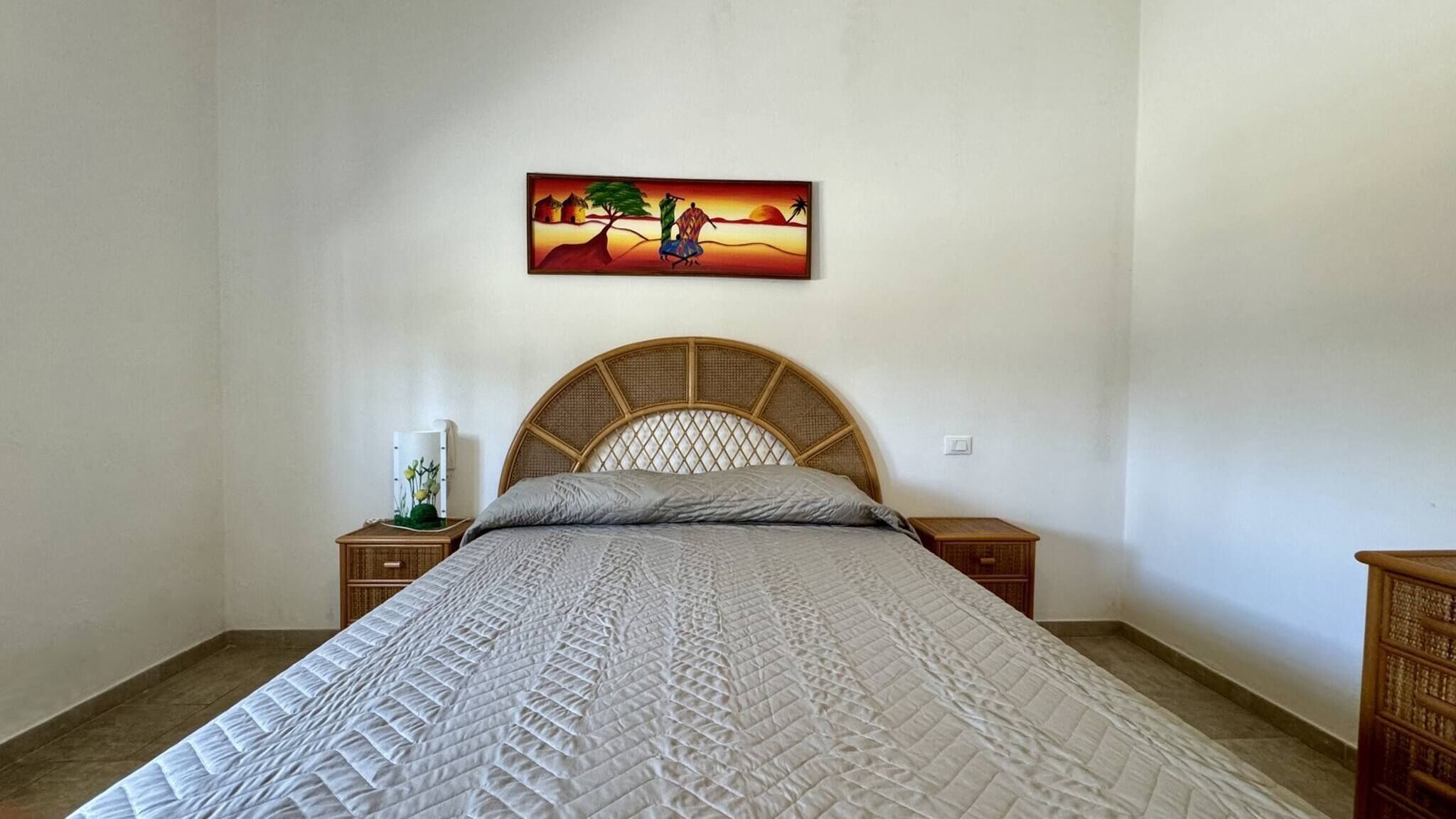 Une chambre à coucher comprenant un lit, une table de chevet, une commode, un tableau accroché au mur et une table de nuit en bois.