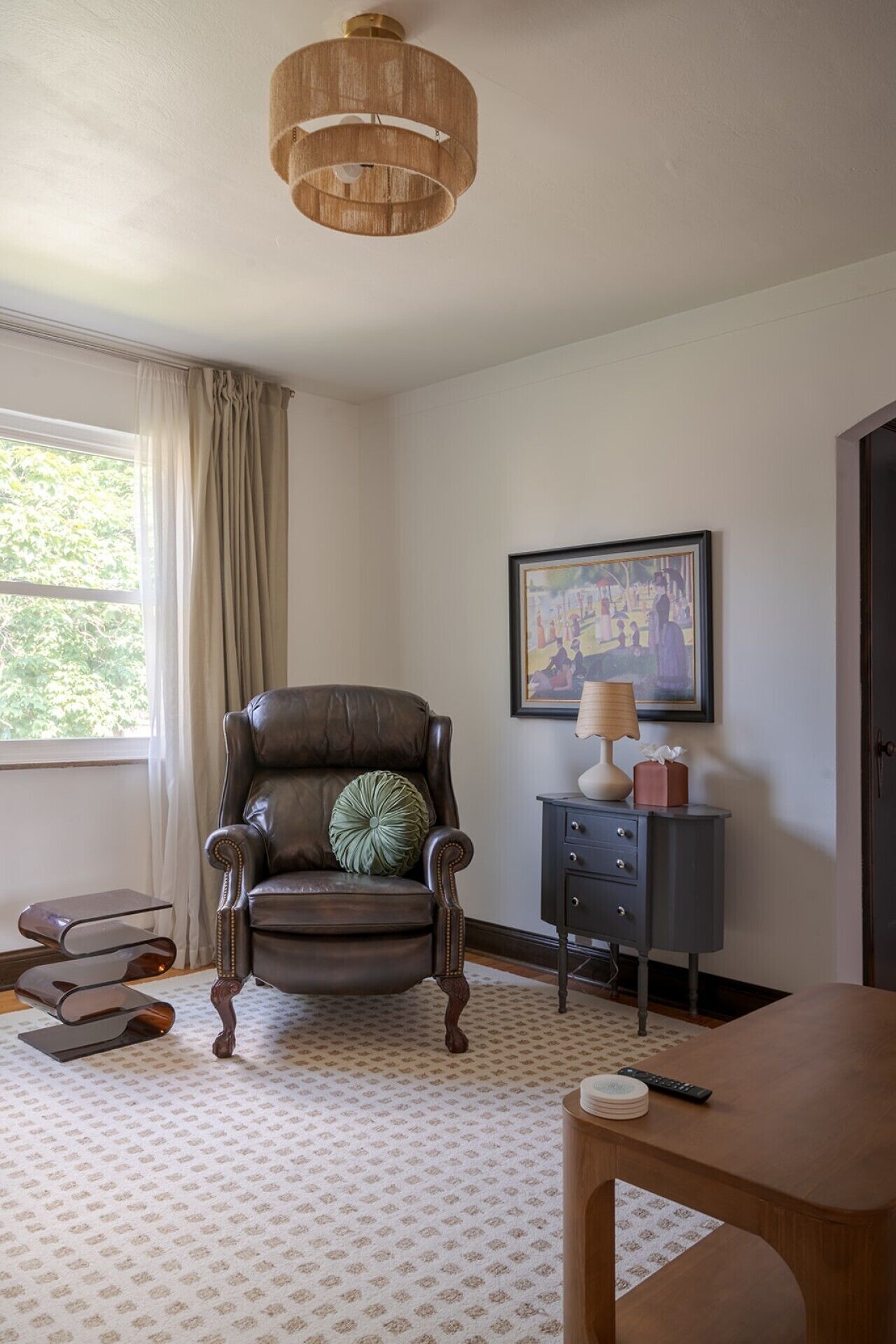 Een kamer met een leren fauteuil, een bijzettafeltje met een lamp, een lijstwerk en een kamerbreed tapijt.