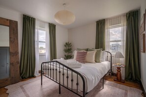 Une chambre à coucher avec un lit, une lampe de chevet, une fenêtre et des rideaux.