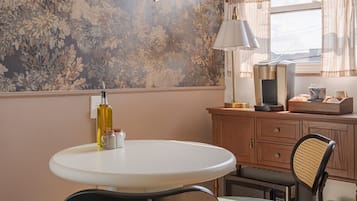 Un coin repas comprenant une table ronde, deux chaises, une machine à café et un mur orné d’un motif floral.