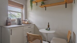 A small kitchen with a window, a table, two chairs, and wooden shelves with plants. - Minutes from OSU Stadium | Walkable | Quiet Area (Columbus)