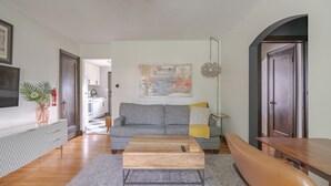A living room with a sofa, coffee table, and a dining table. There is a kitchen in the background. - Minutes from OSU Stadium | Walkable | Quiet Area (Columbus)