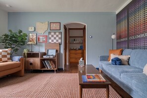 A living room with a blue sofa, a wooden side table, a checkered rug, a bookshelf, and a wall with a Columbus-themed poster. - Free Laundry | Walkable to OSU | Free Parking (Columbus)