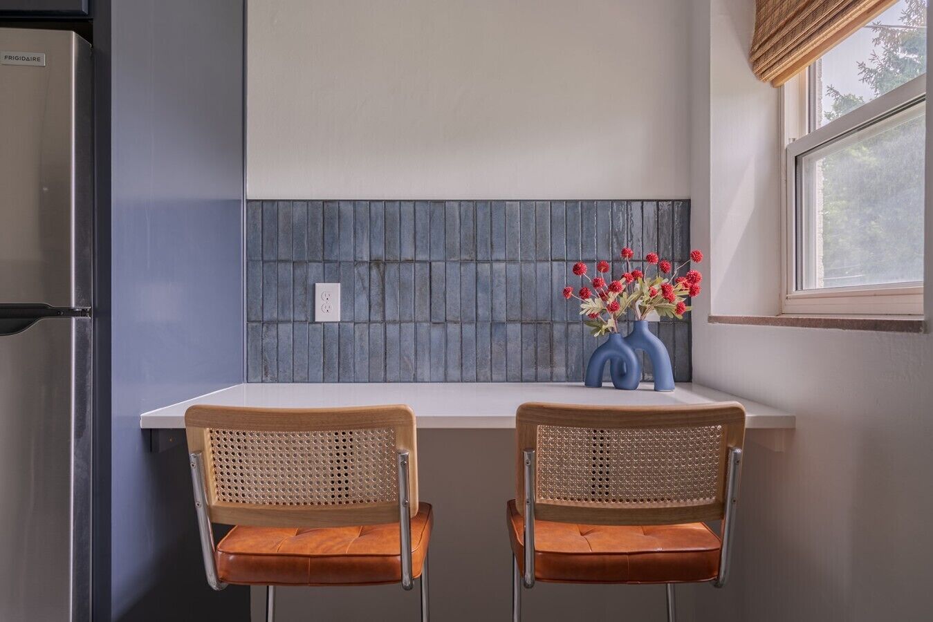 A kitchen with two bar stools, a window with a view, and a backsplash with a grid pattern.