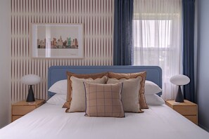 A bedroom with a bed, two bedside tables, a lamp on each table, a wall-mounted artwork, and a window with curtains. - Free Laundry | Walkable to OSU | Free Parking (Columbus)