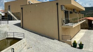 A modern building with a flat roof, a staircase leading to an upper level, and a small outdoor seating area with chairs.