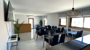 A modern conference room with a large table and chairs, a television on the wall, and a hanging light fixture.