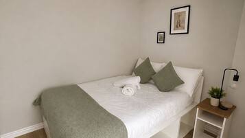 A bedroom with a bed, bedside tables, a hanging light fixture, and a small potted plant.