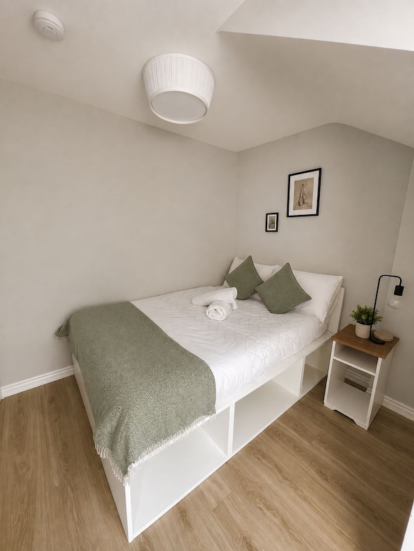 Un dormitorio con una cama, mesitas de noche, una lámpara colgante y una pequeña planta en maceta.