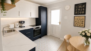 A modern kitchen with white cabinets, a black range hood, and a dining area with a wooden table and chairs. - Super City Centre Location - Sleeps 5 (Galway)