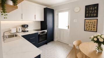 A modern kitchen with white cabinets, a black range hood, and a dining area with a wooden table and chairs.