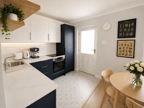 A modern kitchen with white cabinets, a black range hood, and a dining area with a wooden table and chairs.