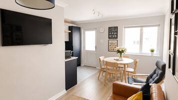A modern living room with a leather sofa, a flat-screen TV, and a dining area with a round table and chairs.